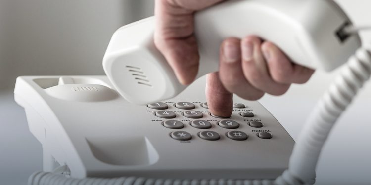 Wide panorama view of a male hand dialing a telephone number in order to make a phone call.